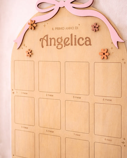 Dettaglio bacheca primo anno bambina in legno — fiocco rosa, fiorellini colorati e nome inciso laser
