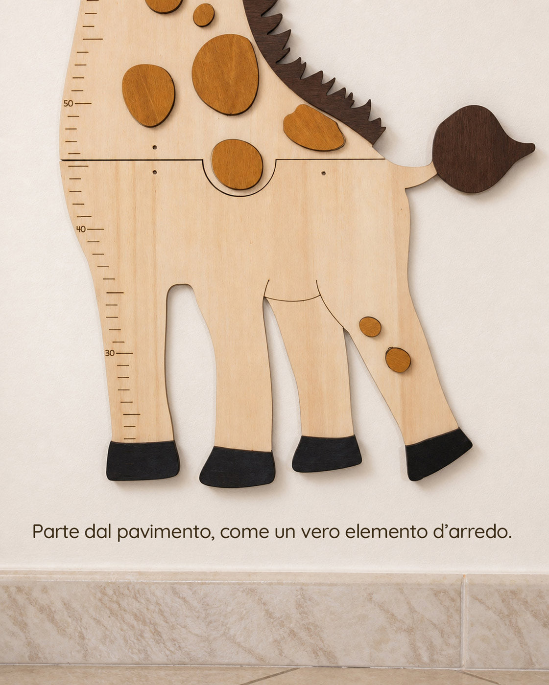 Zampe e coda della giraffa in legno sopra il battiscopa, con la scala da 30 a 50 cm e la scritta: Parte dal pavimento, come un vero elemento d'arredo