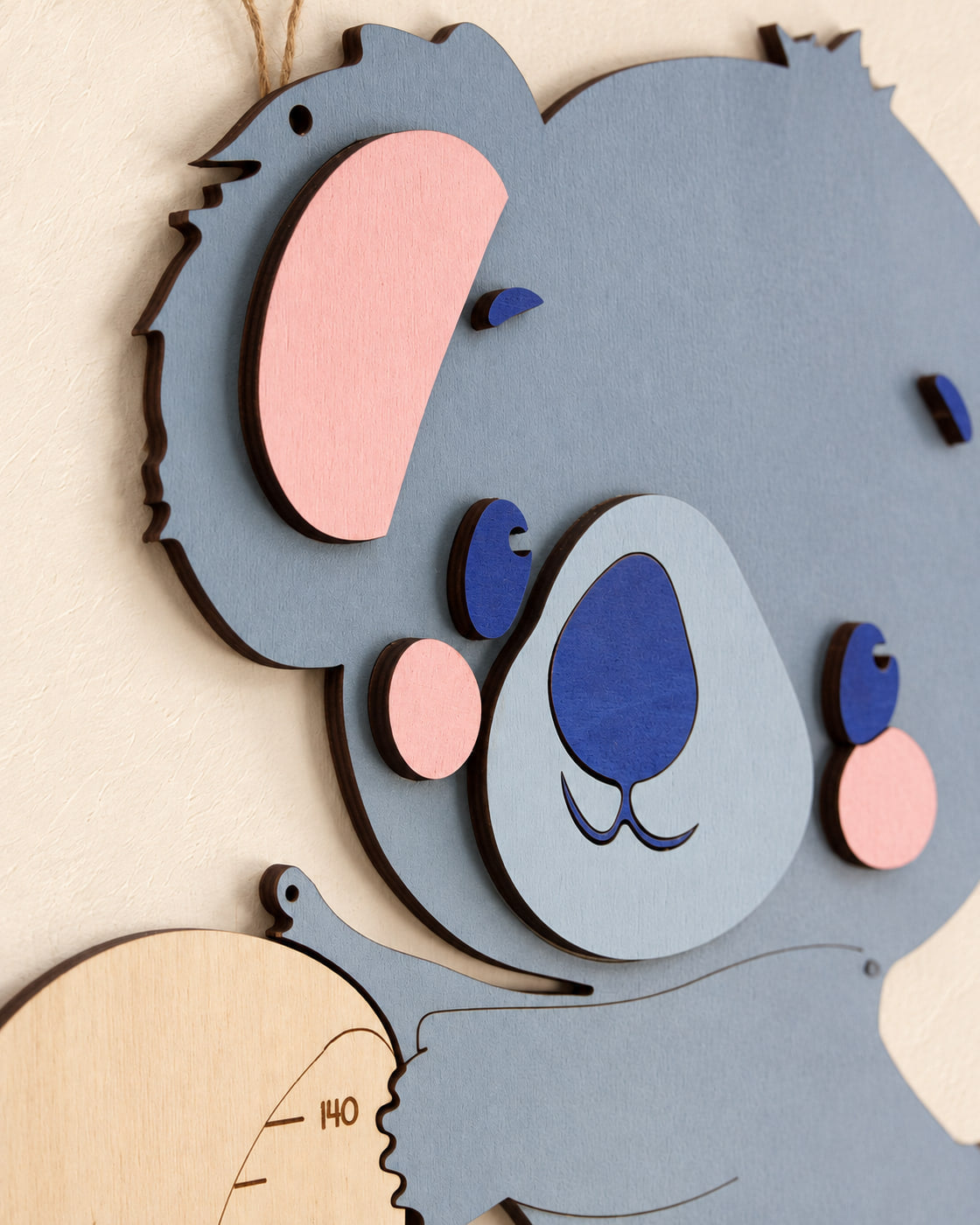 Dettaglio del muso del koala con naso blu, guance rosa e orecchie in legno sovrapposto a rilievo